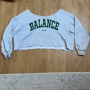 Grå croppad sweatshirt med text - Säljer en grå croppad sweatshirt med texten 'BALANCE WITHIN' i grönt på framsidan. Tröjan har långa ärmar och en avslappnad passform, perfekt för en chill dag. Den är i bra skick och superbekväm att ha på sig. Passar perfekt till jeans eller leggings!
