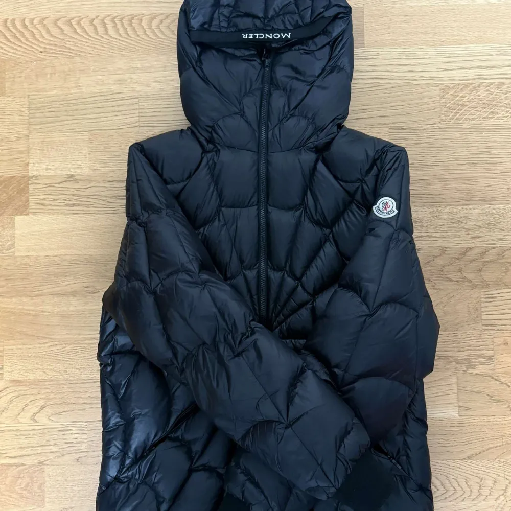 Säljer en snygg svart dunjacka från Moncler i mycket bra skick. Jackan har en cool quiltad design som påminner om ett spindelnät och en praktisk huva. Perfekt för kyliga höst- och vinterdagar. Den har en dragkedja framtill och långa ärmar. Passar både till vardags och lite finare tillfällen.. Jackor.