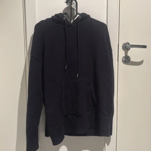 Svart hoodie med ficka - Säljer en svart hoodie i bra skick. Den har en stor ficka framtill och justerbar huva med snören. Perfekt för kyliga dagar eller mysiga hemmakvällar. Passar till det mesta och är superbekväm!