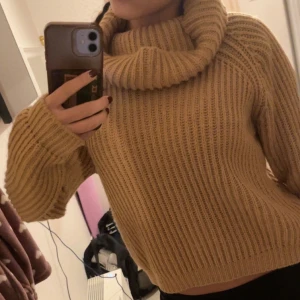 Beige stickad polotröja - Mysig beige stickad polotröja med en stor, gosig krage. Perfekt för kyliga dagar när du vill hålla dig varm och stilren. Tröjan har långa ärmar och en croppad passform som ger en modern touch. Perfekt för höst och vinter!