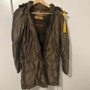 Brun dunjacka med pälsdetaljer - Säljer en brun dunjacka från Parajumpers i mycket bra skick. Jackan har en mysig pälsfodrad huva och praktiska fickor med knappar. Den är långärmad och perfekt för kalla vinterdagar. Dragkedjan är robust och det finns en cool gul detalj vid halsen. Perfekt för både vardag och vinteräventyr! 🧥❄️