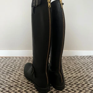 Svarta Primeboots - Snygga svarta Primeboots i skinn med gulddetaljer. Använda enstaka gånger så de är i väldigt gott skick! De har en hög modell med robust sula och. De är i storlek 38 men är stora i storleken så passar även 39-40Passar bra till både vardag och speciella tillfällen✨