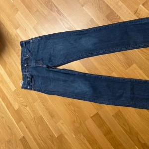 Blå jeans från Levi's - Säljer ett par klassiska blå jeans från Levi's i bra skick. De har en straight/slim passform och är perfekta för både vardag och fest. Jensen har snygg läderpatch med Levi's logga på baksidan. Passar perfekt till en casual look eller med en skjorta för en mer uppklädd stil.