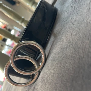 Svart bälte med silverdetaljer - Snyggt svart bälte i skinn med dubbla silverringar som spänne. Perfekt för att ge en stilren touch till vilken outfit som helst. Passar både till vardags och fest. Bältet är i mycket bra skick och har en klassisk design som aldrig går ur tiden.