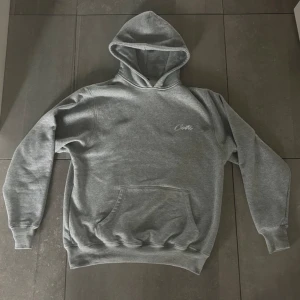 Corteiz hoodie - Säljer en grå hoodie från Corteiz i storlek medium. Den är supermjuk och perfekt för kyliga dagar🥶Hoodien har en klassisk passform med en stor ficka fram och en broderad logga på bröstet. Perfekt för både vardag och chill.