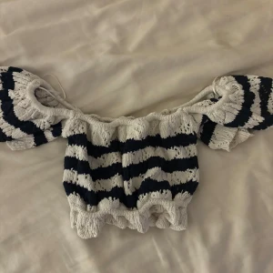 Randig offshoulder topp - Säljer en superfin randig offshoulder topp i blått och vitt. Den är croppad och har volangdetaljer vid ärmslut och nederkant. Perfekt för sommardagar eller en festlig kväll. Toppen är i mycket bra skick