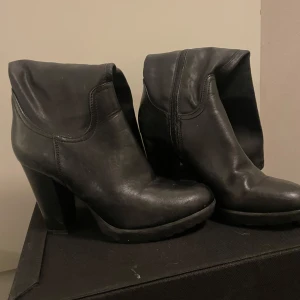 Svarta boots med klack - Snygga svarta boots i skinn med hög klack och dragkedja på sidan. Perfekta för höst och vinter, dessa boots ger en stilren look och passar både till vardags och fest. De har en rund tå och är i bra skick.