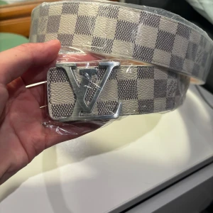 Rutig bälte med silverdetaljer - Säljer ett snyggt rutig bälte i vitt. Bältet har en stilren design med en stor silverfärgad spänne. Perfekt för att ge din outfit en lyxig touch. Bältet är i nytt skick och kommer i originalförpackning.