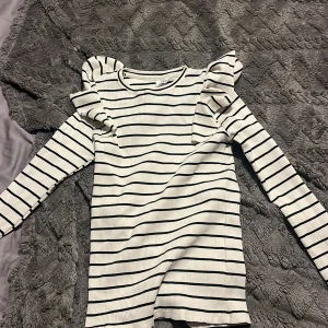 Randig tröja med volangdetaljer från Zara - Säljer en superfin randig tröja från Zara i storlek 13-14 år. Den är vit med svarta ränder och har coola volangdetaljer på axlarna. Perfekt för både vardag och fest! Tröjan är i nyskick och gjord av ett mjukt, ribbat material. Den har inte använts innan!🥰Skriv till mig om frågor & fler bilder❤️