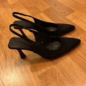 Svarta pumps från Stradivarius - Snygga svarta pumps från Stradivarius i mycket bra skick. De har en elegant spetsig tå och en smal klack som ger en stilren look. Perfekta för festliga tillfällen eller en utekväll. Bekväma och lätta att matcha med olika outfits.