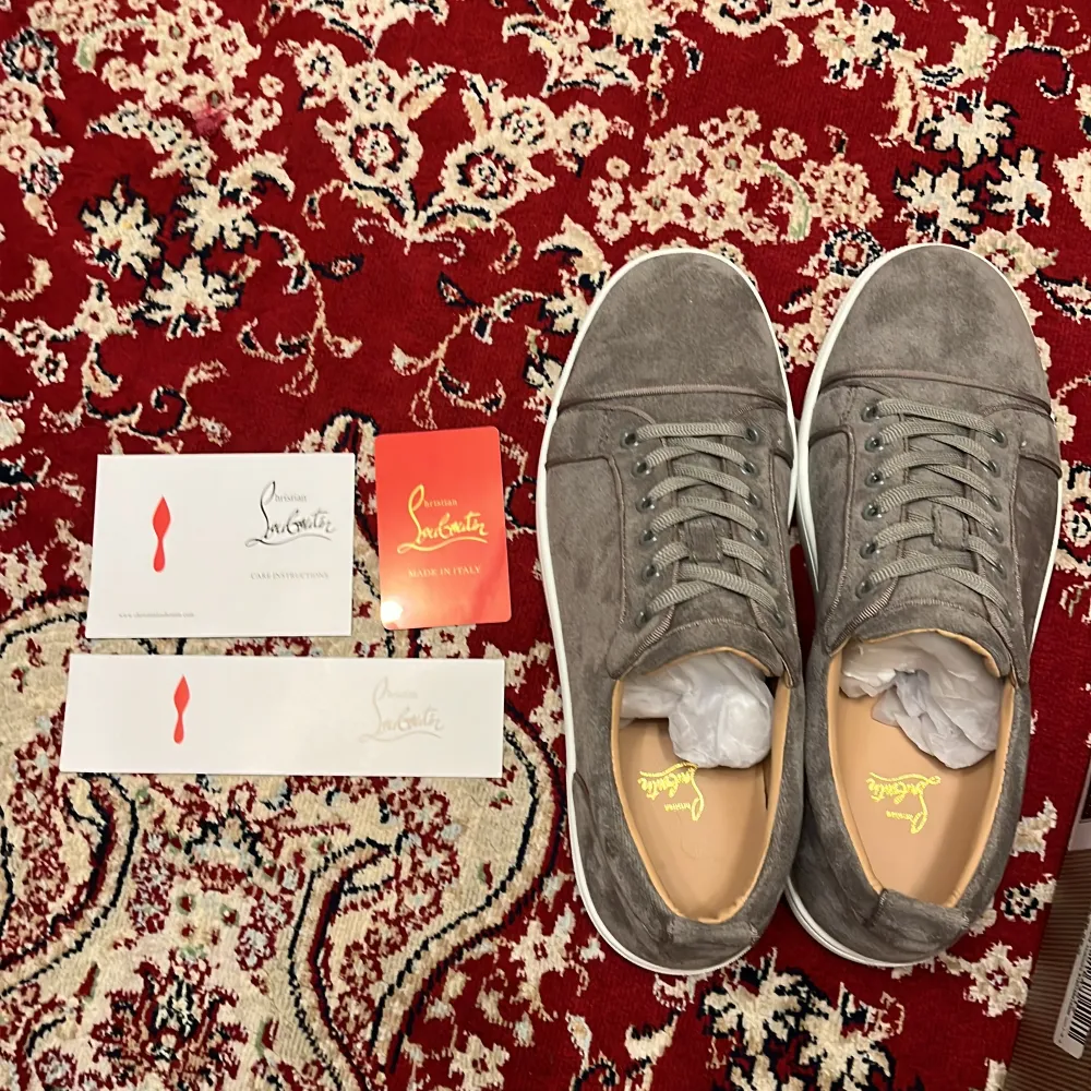 Säljer ett par snygga grå sneakers från Christian Louboutin i mocka. De har den ikoniska röda sulan och är i mycket bra skick. Perfekta för både vardag och fest! Skorna har snörning och en stilren design som passar till det mesta.. Skor.