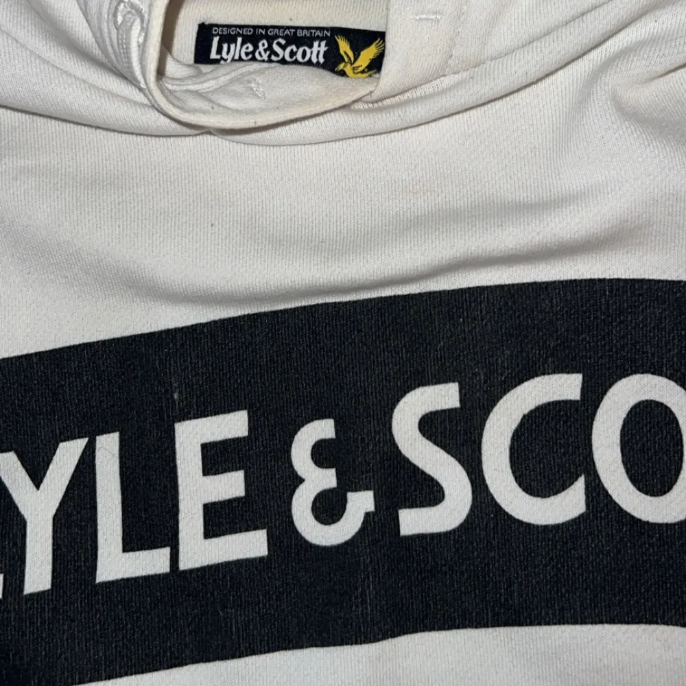 Säljer en snygg vit hoodie från Lyle & Scott. Den har en stor logga på bröstet och en klassisk känguruficka. Perfekt för en avslappnad stil och passar till alla årstider. Skön och stilren design!. Tröjor & Koftor.