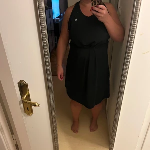 Svart klänning från She Did - Snygg svart klänning från She Did i storlek XXL. Den är ärmlös och har en elegant design med ett knytband i midjan som ger en fin passform. Perfekt för både vardag och festliga tillfällen. Klänningen är i mycket bra skick och redo att bäras av dig!