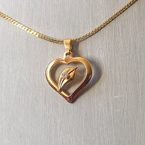 Guldhalsband med hjärthänge - Säljer ett elegant guldhalsband med ett hjärtformat hänge. Hänget har en fin detalj i form av ett löv med en gnistrande sten i mitten. Perfekt för att ge en touch av romantik till din outfit. Kedjan är tunn och smidig, vilket gör den bekväm att bära hela dagen. Okänd metall 