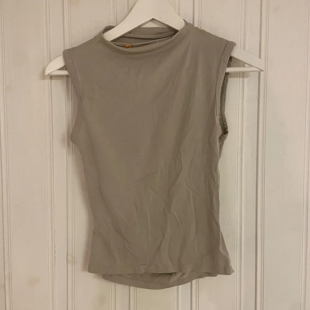 Snygg beige ärmlös topp i ett mjukt och stretchigt material. Perfekt för sommardagar eller som ett lager under en jacka. Toppen har en enkel design med en lätt rynkad detalj på sidan för en smickrande passform.. Toppar.