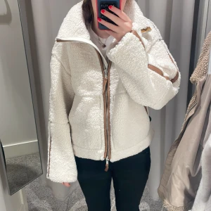Vit teddyjacka från H&M - Mysig vit teddyjacka från H&M med bruna detaljer och dragkedja. . Jackan har långa ärmar och en hög krage för extra värme.