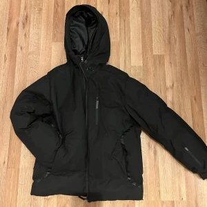 J&J Svart Dunjacka med huva - Snygg och varm svart dunjacka med huva. Jackan har dragkedja framtill och praktiska fickor med dragkedjor. Perfekt för kyliga dagar. Inköpt på J&J för 1500kr och är endast använd ett fåtal gånger.