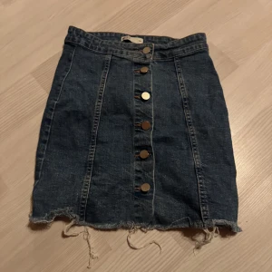 Jeanskjol från gina  - Snygg jeanskjol från gina tricot med knappar framtill. Kjolen har en rå kant nertill för en trendig look. Perfekt för en avslappnad stil.