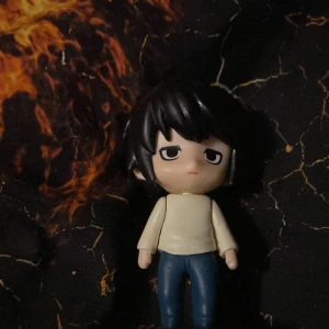 Animefigur med svart hår och vita kläder - En söt animefigur med svart hår och en neutral ansiktsuttryck. Figuren bär en vit tröja och blå byxor, och står på en vit rund bas. Perfekt för samlare av animeprylar eller som dekoration.