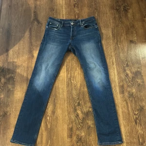 Blå jeans från Jack & Jones - Snygga blå jeans från Jack & Jones med klassisk femficksdesign och knappgylf. Perfekta för en avslappnad stil med en straight passform som funkar till det mesta.