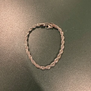 Silverfärgat tvinnat armband - Elegant silverfärgat armband med tvinnad design. Perfekt för att ge en stilren touch till din outfit. Armbandet har en säker låsning och passar de flesta handleder.