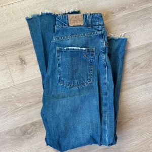 Blå jeans - Snygga blå jeans. Jeansen har en rak passform och är perfekta för en avslappnad stil. De har en knappgylf och en liten slitsdetalj vid bensluten.