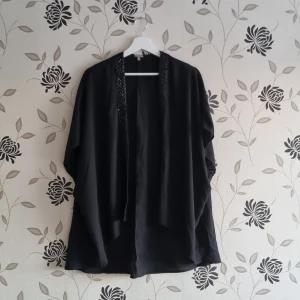 Svart blus med paljettkant i fram, Strl: Xs/34/one size - Elegant svart kavaj från Charlotte Russe, med glittrande paljettkant. Perfekt för att lägga till lite glamour till din outfit. Kavajen har en öppen design och är tillverkad i ett lätt material. Storlek Xs men passar även större storlekar.