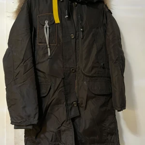 Svart parkajacka från Parajumpers - Säljer en svart parkajacka från Parajumpers med pälsdetaljer på huvan. Jackan har flera fickor, dragkedja och knappar framtill. Perfekt för kalla vinterdagar med sin robusta design och varma foder.