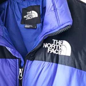 Lila och svart dunjacka från The North Face - Säljer en lila och svart dunjacka från The North Face. Jackan har en dragkedja framtill och två sidofickor. Den är perfekt för kallt väder och har en klassisk pufferdesign med långärmade ärmar.