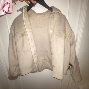 Beige jacka från & Other Stories - Snygg beige jacka från & Other Stories med knappar och två bröstfickor. Jackan är tillverkad i en blandning av alpacka, ull och polyester, vilket ger en mjuk och varm känsla. Perfekt för höst och vår