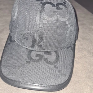 Svart keps från Gucci - Snygg svart keps från Gucci med det ikoniska GG-mönstret. Kepsen har en justerbar rem baktill för perfekt passform. Perfekt accessoar för en stilren look.