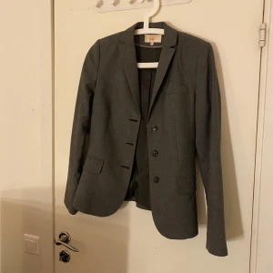 Grå kavaj från Riley - Snygg grå kavaj från Riley i storlek 36. Kavajen har en klassisk design med tre knappar framtill och fickor. Perfekt för en stilren look.