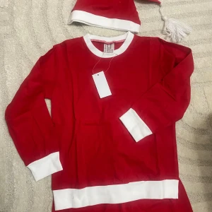 Röd tomtedräkt med luva - Säljer en röd tomtedräkt med vita detaljer och matchande luva. Perfekt för julfirandet! Dräkten har långa ärmar och byxor med elastiska muddar. Tillverkad i mjukt material för extra komfort.