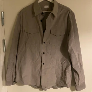 Tiger of Sweden skjorta ARNOU - Grå/beige skjorta i 100% bomullsmanchester från Tiger of Sweden. Den är i storlek L & har använts som  en overshirt. Väldigt sparsamt använd & utan defekter!                                                                      Nypris: 1 799kr