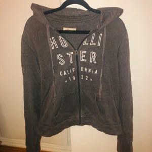 Grå hoodie från Hollister - Säljer en grå hoodie från Hollister med dragkedja och tryck framtill. Den har en justerbar huva och praktiska fickor. Säljer pågrund av att den inte är min still. Är i bra skick❤️