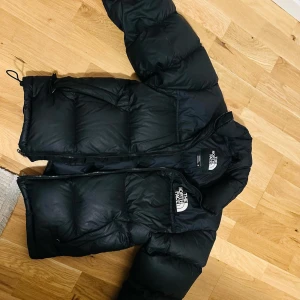 Svart dunjacka från The North Face - Säljer en svart dunjacka från The North Face. Jackan har en pufferdesign med dragkedja och långa ärmar. Perfekt för kalla dagar.