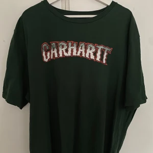 Grön t-shirt från Carhartt - Säljer en grön t-shirt från Carhartt med ett stort tryck på framsidan. T-shirten har en avslappnad passform och är perfekt för en casual look. 