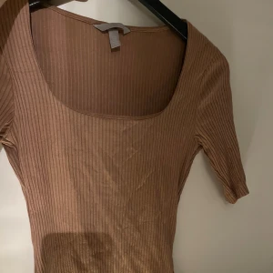Beige ribbad topp - Beige basic ribbad topp med korta ärmar och rund halsringning. Extra tyg innanför. Väldigt stretchig i materialet. Använt max 2-3 gånger.