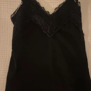 Svart linne med spetsdetaljer - Super sött svart linne med spetsdetaljer och tunna axelband. Perfekt som pyjamas topp eller till vardags💕