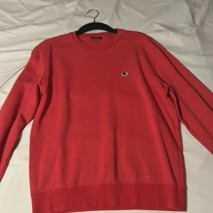 Röd sweatshirt från Champion - Säljer en klassisk röd sweatshirt från Champion med rund hals och det ikoniska Champion-logotypen på bröstet. Tröjan har långa ärmar och är perfekt för en avslappnad stil.