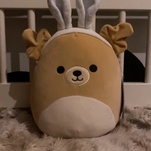 Squishmallow Stevon med kaninöron - Mjuk och gosig Squishmallow vid namn Stevon. Den har ett gulligt ansikte med kaninöron och en rund kropp i beige och vit färg. Perfekt för kramar och dekoration. Den har en pytte liten defekt men går bort o tvätten men annars syns den knappt den e limited edition köpte den i påskas (pris kan diskuteras ❤️)
