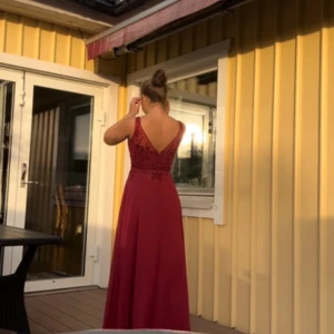 Vinröd långklänning med spetsdetaljer - Elegant vinröd långklänning från Morilee Madeline Gardner med spetsdetaljer och v-ringning. Klänningen har en öppen rygg och smala axelband, perfekt för bal. Helt oanvänd då jag valde att ha min andra balklänning. Extra delar så som paljetter och tyg får man med ifall något skulle gå sönder. Storlek 40 men skulle säga mer åt 38 hållet. Köpt för 3499kr 