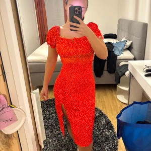 Röd prickig klänning med slits ❤️ - Trendig röd klänning med vita prickar och en smickrande slits framtill. Klänningen har korta ärmar och en söt knytning vid bysten. Perfekt för en somrig look!
