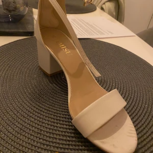 Beige sandaler med klack - Stilrena beige sandaler från Nelly med öppen tå och blockklack. Perfekta för sommarens alla tillfällen. Justerbart spänne runt ankeln för bästa passform.