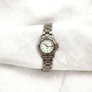 Ellen : Tvåfärgad klocka från Pierre Lannier - Elegant klockan Ellen från Pierre Lannier med en stilren design. Armbandet är i tvåfärgad metall med silver och guldtoner. Urtavlan är vit med tydliga siffror och datumvisning. Perfekt för både vardag och speciella tillfällen. Omkrets: 18,2cm , Urets bredd: 2,8 cm , Längden: 26 cm . Går att förminska (ta bort länk) hos urmakare. 