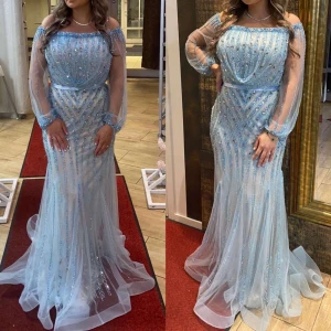 Ljusblå glittrig långklänning - Elegant ljusblå långklänning med glittriga detaljer och offshoulder-design. Klänningen har långa, transparenta ärmar och en smickrande passform med ett bälte i midjan. Perfekt för speciella tillfällen.