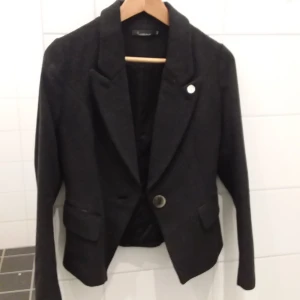 Svart kavaj från Ambre des Sables - Elegant svart kavaj med klassisk design från Ambre des Sables. Kavajen har långa ärmar och stängs med en knapp framtill. Perfekt för en stilren look.