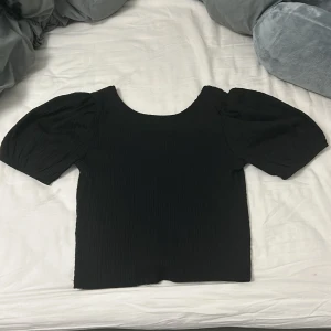 Svart topp från 1st7 - Snygg svart topp från 157 med puffiga kortärmar och en rund halsringning. Perfekt för en stilren look.