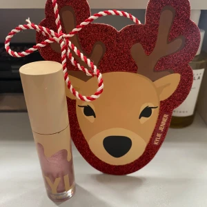 Kylie Jenner High Gloss (323 daddy’s girl) - Säljer en Kylie Jenner High Gloss i en skimrande rosa nyans. Förpackningen har en söt julig renmotiv med glitter och rödvit snöre som man kan hänga upp som julgranspynt. Perfekt för att ge läpparna en glansig finish.