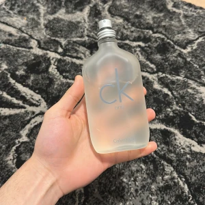 CK One Eau de Toilette - Säljer en klassisk CK One Eau de Toilette från Calvin Klein. Flaskan är frostad och har en minimalistisk design med en grå spraykork. Perfekt för den som gillar en fräsch och unisex doft.